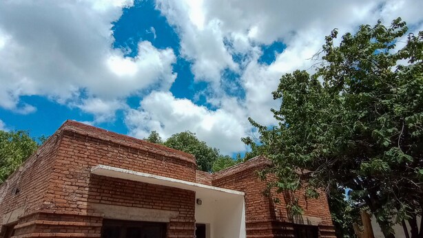 A brick building with a white door and windows, surrounded by trees and a clear sky. - casa nuestra hostal (Salta)