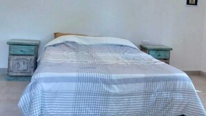 A single bed with a striped bedspread in a room with white walls and two nightstands. - casa nuestra hostal (Salta)