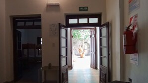 A hallway with a checkered floor, a fire extinguisher, and an emergency exit sign. - casa nuestra hostal (Salta)