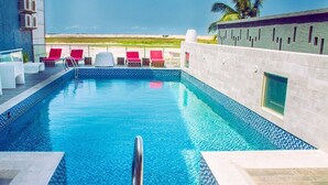 A swimming pool with clear blue water, surrounded by white lounge chairs and a glass railing. - MountRoyal Centre Hotel and Suites (Lagos)
