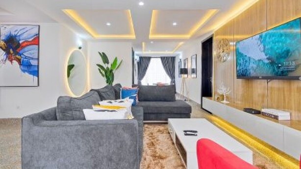 A modern living room with a grey sofa, a red chair, a coffee table, and a TV mounted on the wall. - MountRoyal Centre Hotel and Suites (Lagos)
