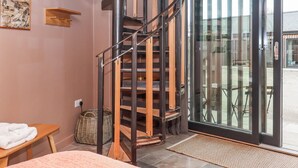 A spiral staircase with a wooden finish, a glass door leading outside, a wicker basket, and a small wooden table with a towel. - 3 Caddaford Barns (Buckfastleigh)