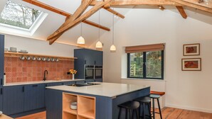A modern kitchen with a central island, wooden beams, and a skylight. - 3 Caddaford Barns (Buckfastleigh)