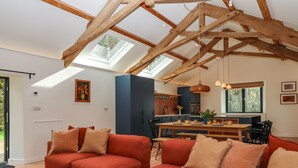 A spacious living area with a high ceiling and exposed wooden beams, a cozy red sofa set, a dining table with chairs, and a view of the outdoors through skylights. - 3 Caddaford Barns (Buckfastleigh)