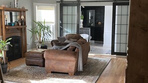 A spacious living room with a brown leather sofa, a wooden coffee table, and a large window. - Chester County Oasis with Pool, Modern Ammenities, Tranquil and Private (West Chester)