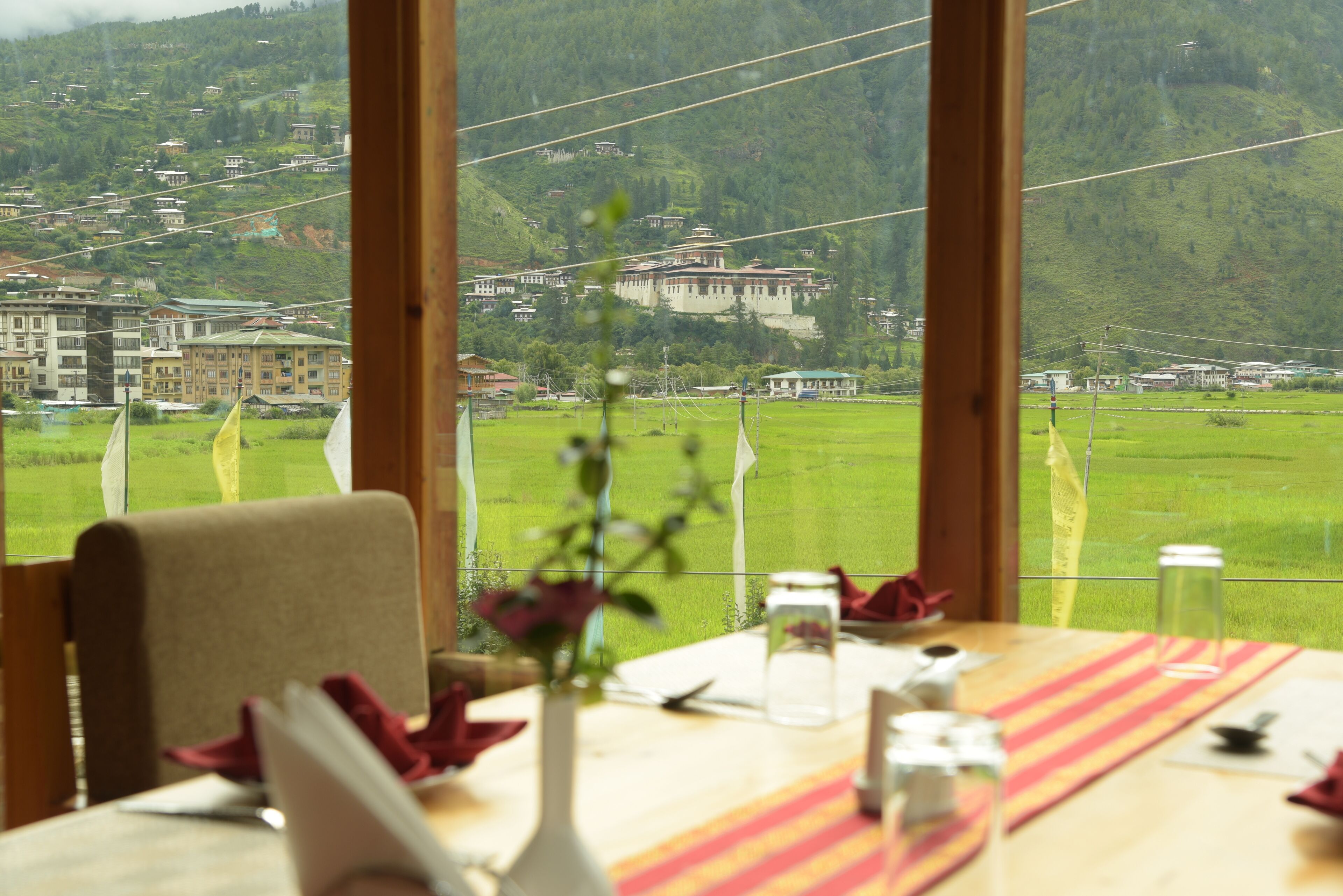 A dining table with a view of a green field and buildings in the distance.