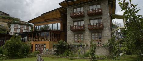 A multi-story building with balconies, a garden area with a wooden structure, and a stone wall.