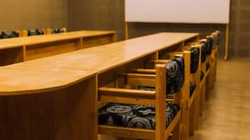 Un salón de conferencias con largas mesas de madera y sillas con cojines estampados.