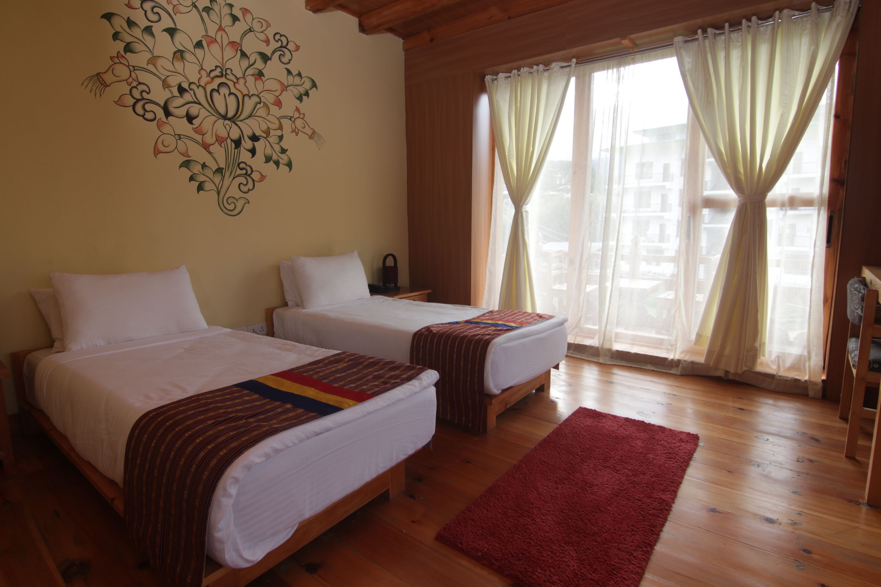 Une chambre avec deux lits, un tapis rouge et une fenêtre avec des rideaux.