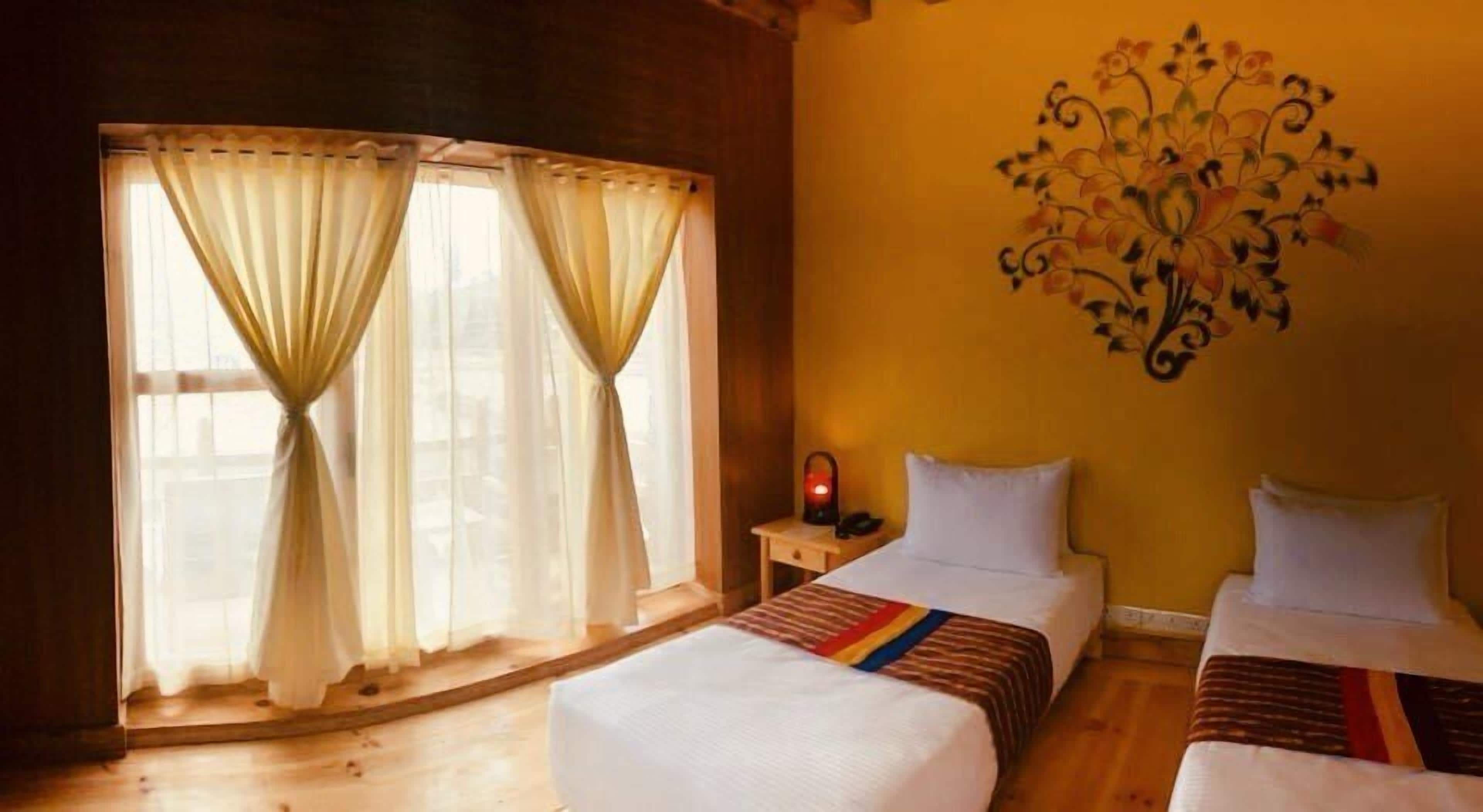 A room with two beds, a nightstand, a lamp, and a wall decoration.