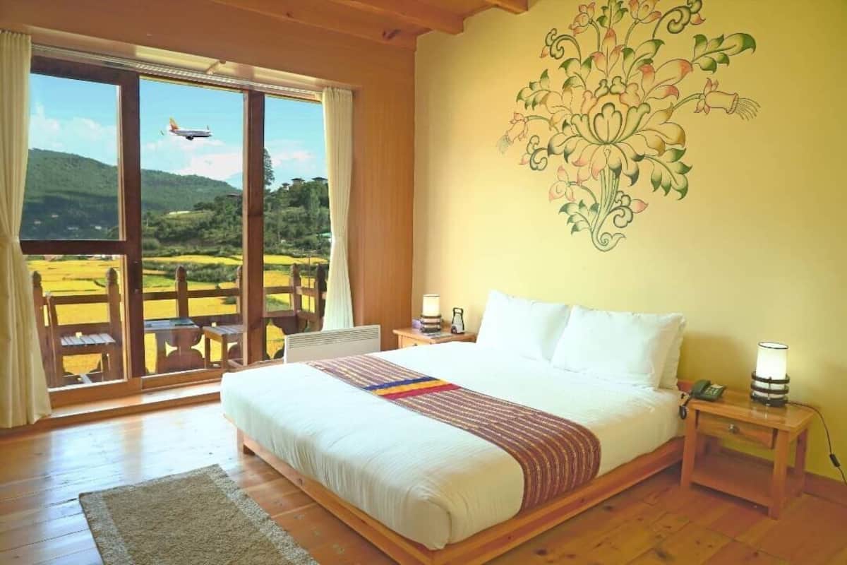 Ein Schlafzimmer mit einem großen Bett, einem Nachttisch, einer Lampe und Blick auf eine grüne Landschaft durch eine Schiebetür.