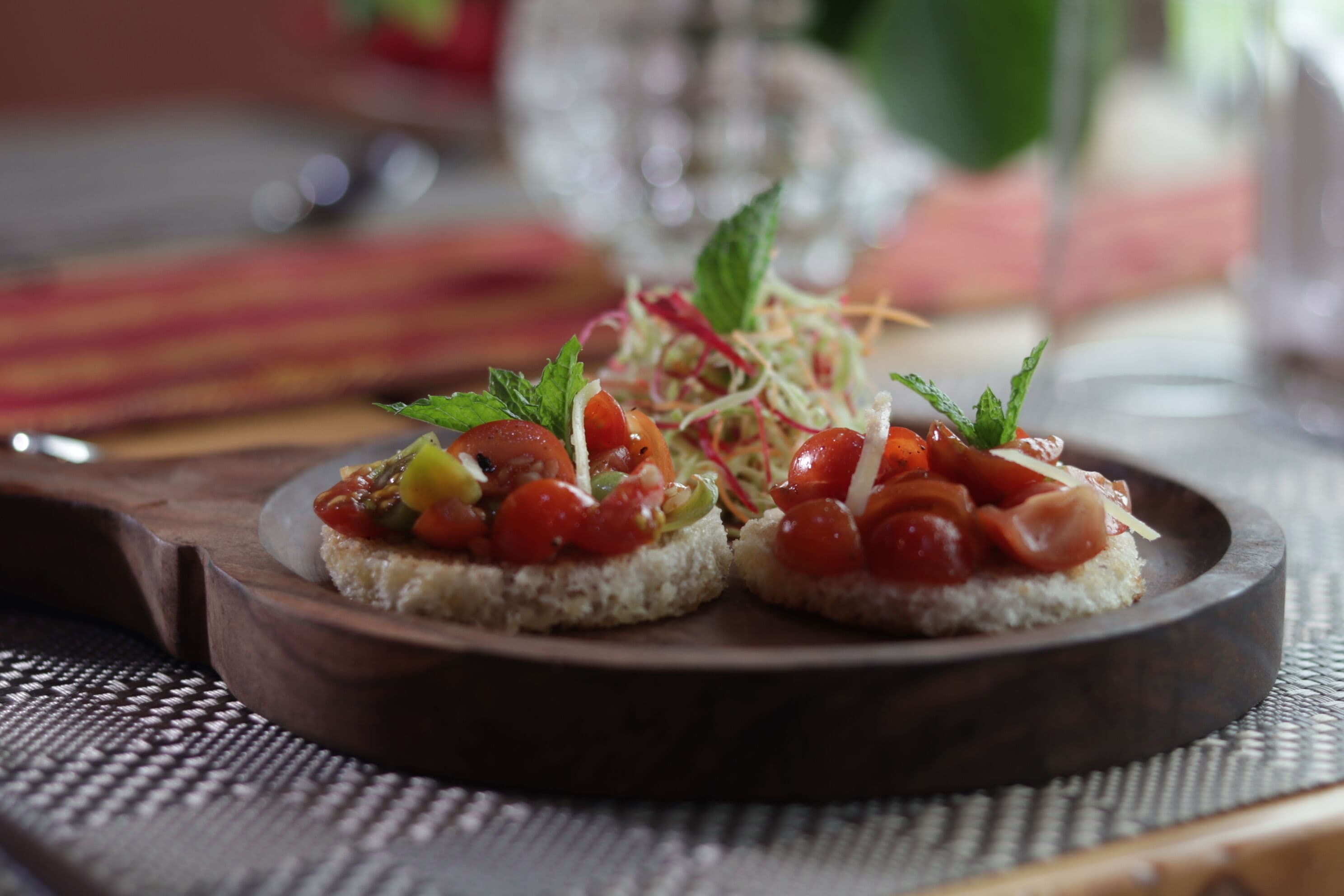 Dos pequeños aperitivos sobre un plato de madera, adornados con hierbas y verduras.