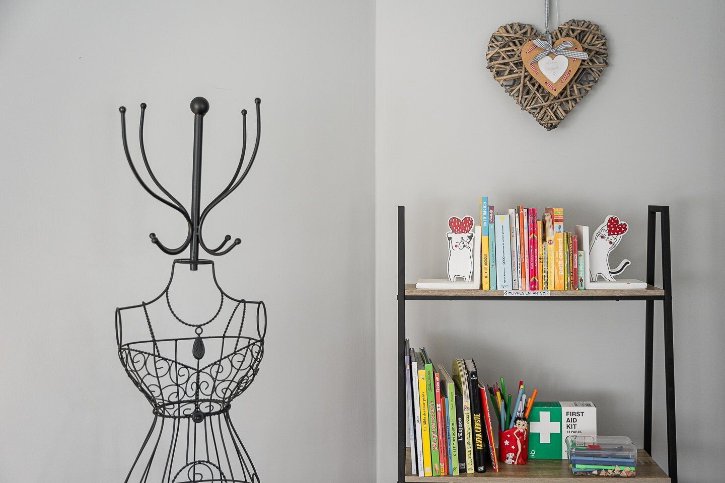 Een kamer met een metalen wandsculptuur van een jurk en een boekenkast met boeken en een verbanddoos.