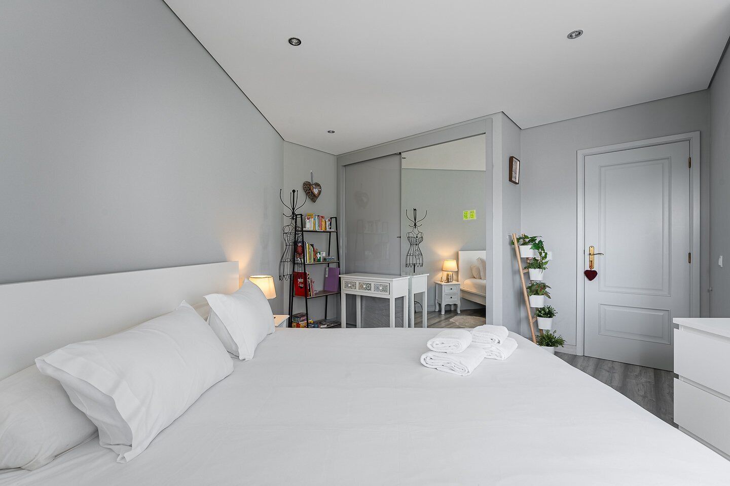 A modern hotel room with a large bed, a desk, a chair, and a wardrobe.