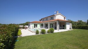 A two-story house with a swimming pool, a covered patio, and a well-maintained lawn.