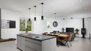 A modern kitchen with a central island, dining area with a wooden table and chairs, and a television.