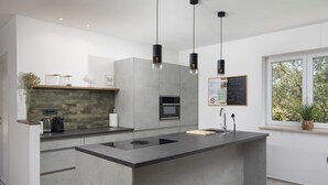 A modern kitchen with a central island, built-in appliances, pendant lighting, and a window with a view.