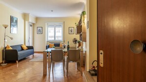 Una sala de estar moderna con sofá, mesa de comedor y sillas. El piso es de madera y hay una puerta a la derecha.