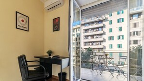 Una habitación con escritorio, silla y un ventanal que da a un balcón con mobiliario exterior.