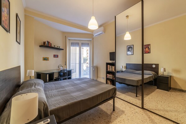 A bedroom with a bed, bedside tables, a desk with a chair, a bookshelf, and a mirror.