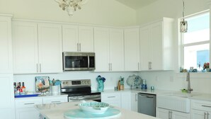Una cocina moderna con muebles blancos, una isla central con taburetes, una lámpara de araña y una ventana con vistas.