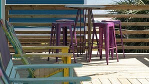 Una terraza de madera con sillas Adirondack de colores y una mesa, con vista a un cuerpo de agua.