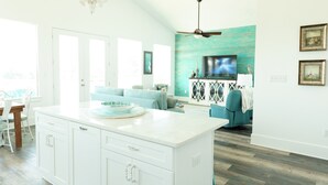 Una cocina amplia con una isla grande, un comedor con mesa y sillas, y una sala de estar con sofá y televisor.