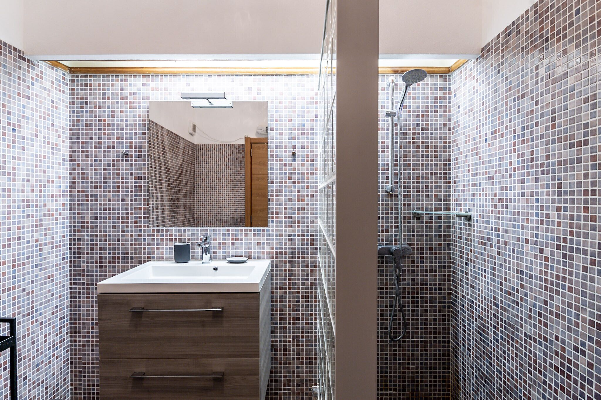 A bathroom with a tiled mosaic wall, a wooden vanity with a sink, and a shower area.