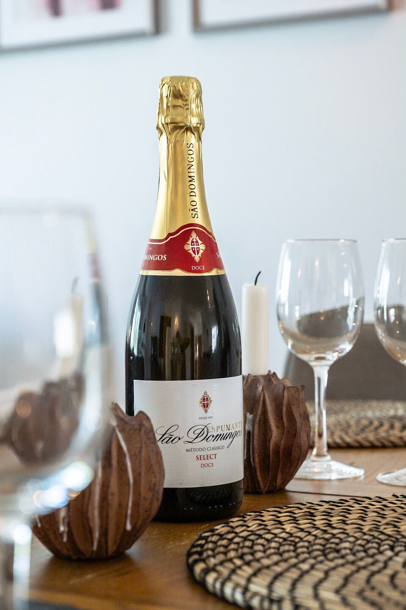 A bottle of São Domingos wine with a label, two glasses, and a candle on a table.