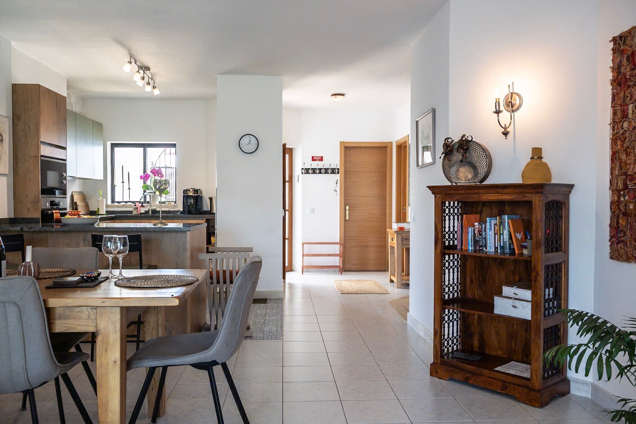 Een moderne keuken met een eethoek, een houten boekenkast en een klok aan de muur.