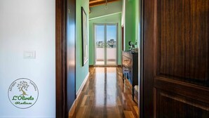 Un pasillo con piso de madera, una puerta de madera y vistas a un balcón exterior.