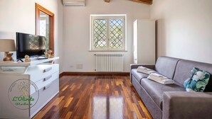 Un salón amplio con techo de madera, un televisor sobre un aparador blanco, un sofá gris y una ventana con celosía decorativa.