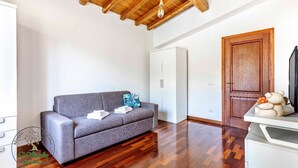 Una habitación con un sofá gris, suelo de madera, un armario blanco y una puerta de madera.
