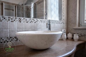 Ein Badezimmer mit einem großen, ovalen Waschbecken in Weiß, einer Duschkabine aus Glas und einer gefliesten Rückwand.
