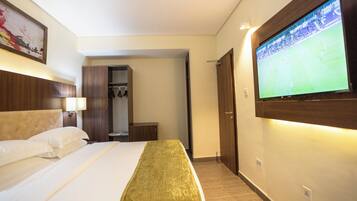 Habitación de hotel con cama, televisión en la pared, armario y puerta que da a otra habitación.
