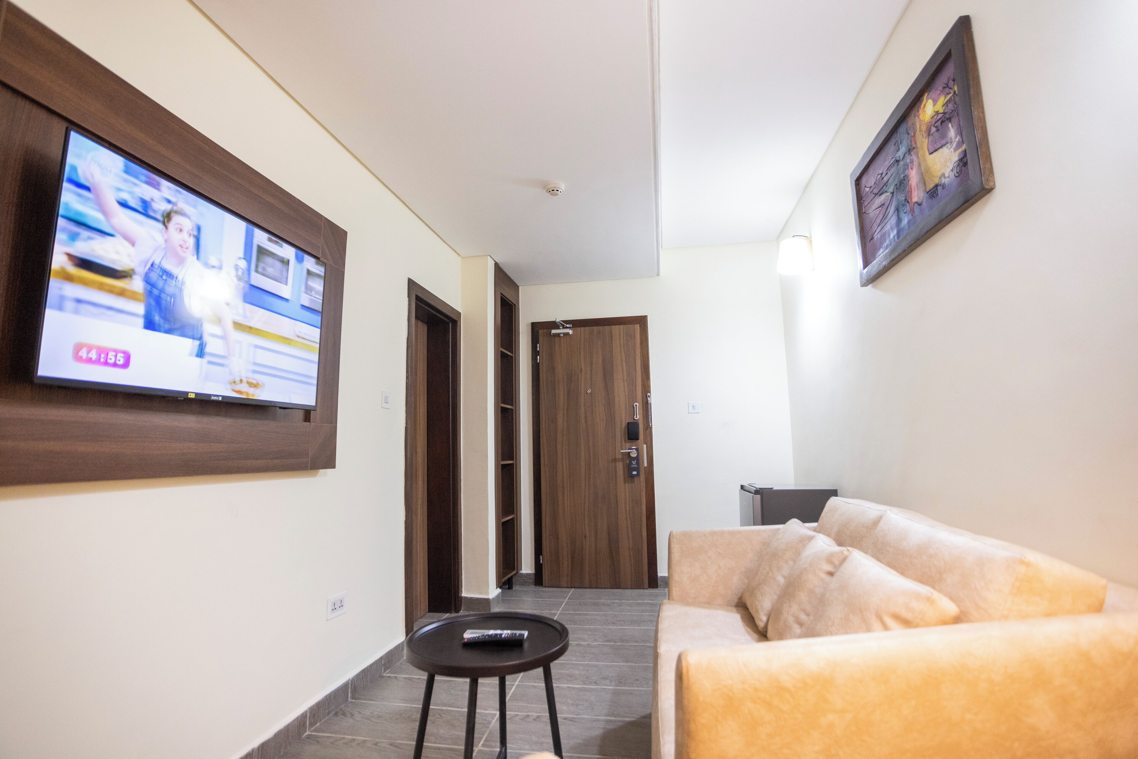 Sala de estar com televisão na parede, sofá, mesinha e uma porta que dá para outro cômodo.