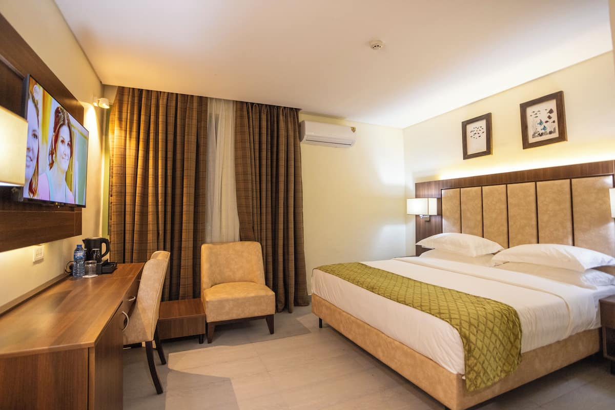 A hotel room with a bed, a desk, a chair, an air conditioning unit, and a television.