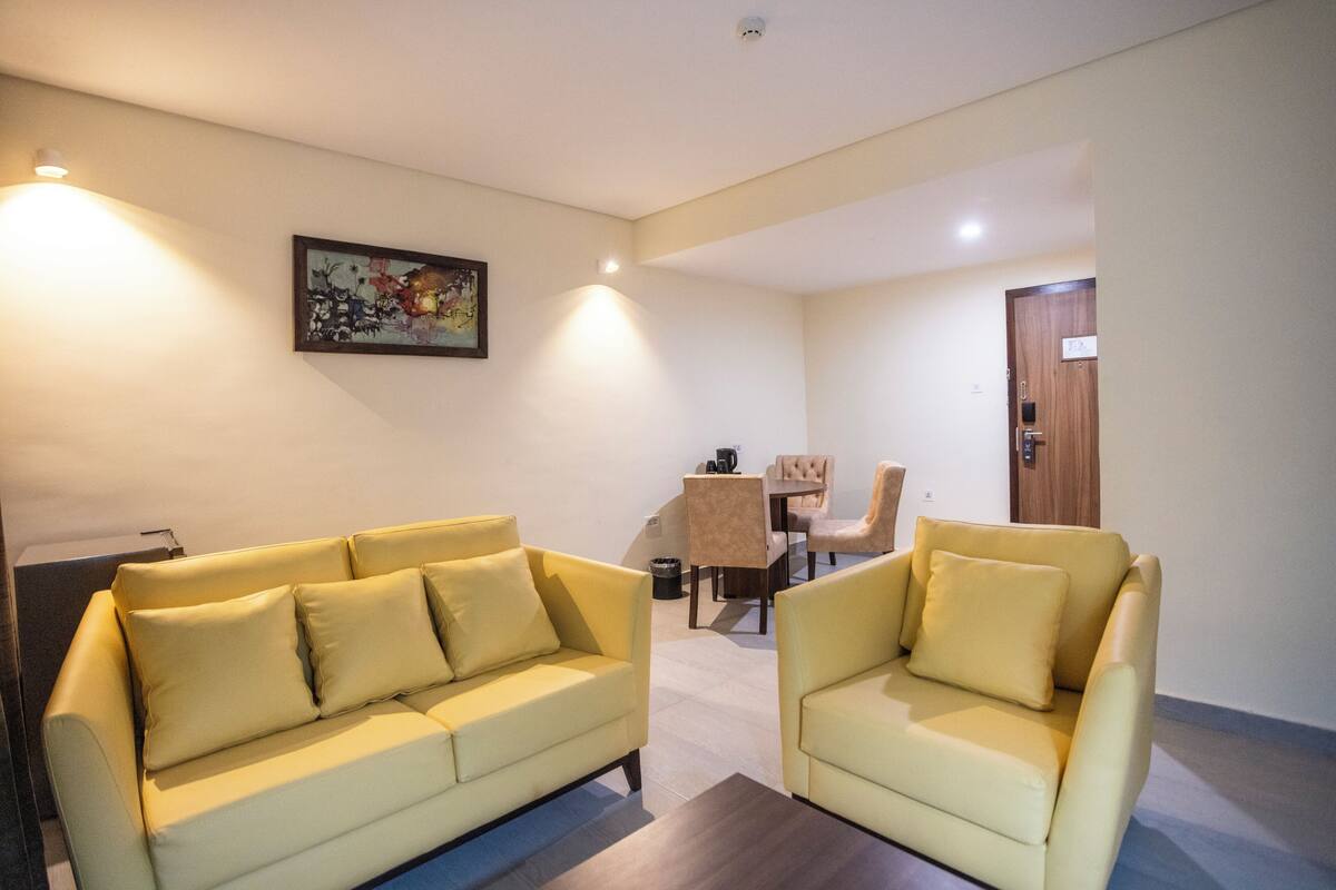 A modern living room with two yellow sofas, a dining table with chairs, and a painting on the wall.