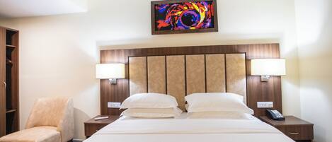 A hotel room with a bed, two bedside lamps, a chair, a painting on the wall, and a telephone on the nightstand.