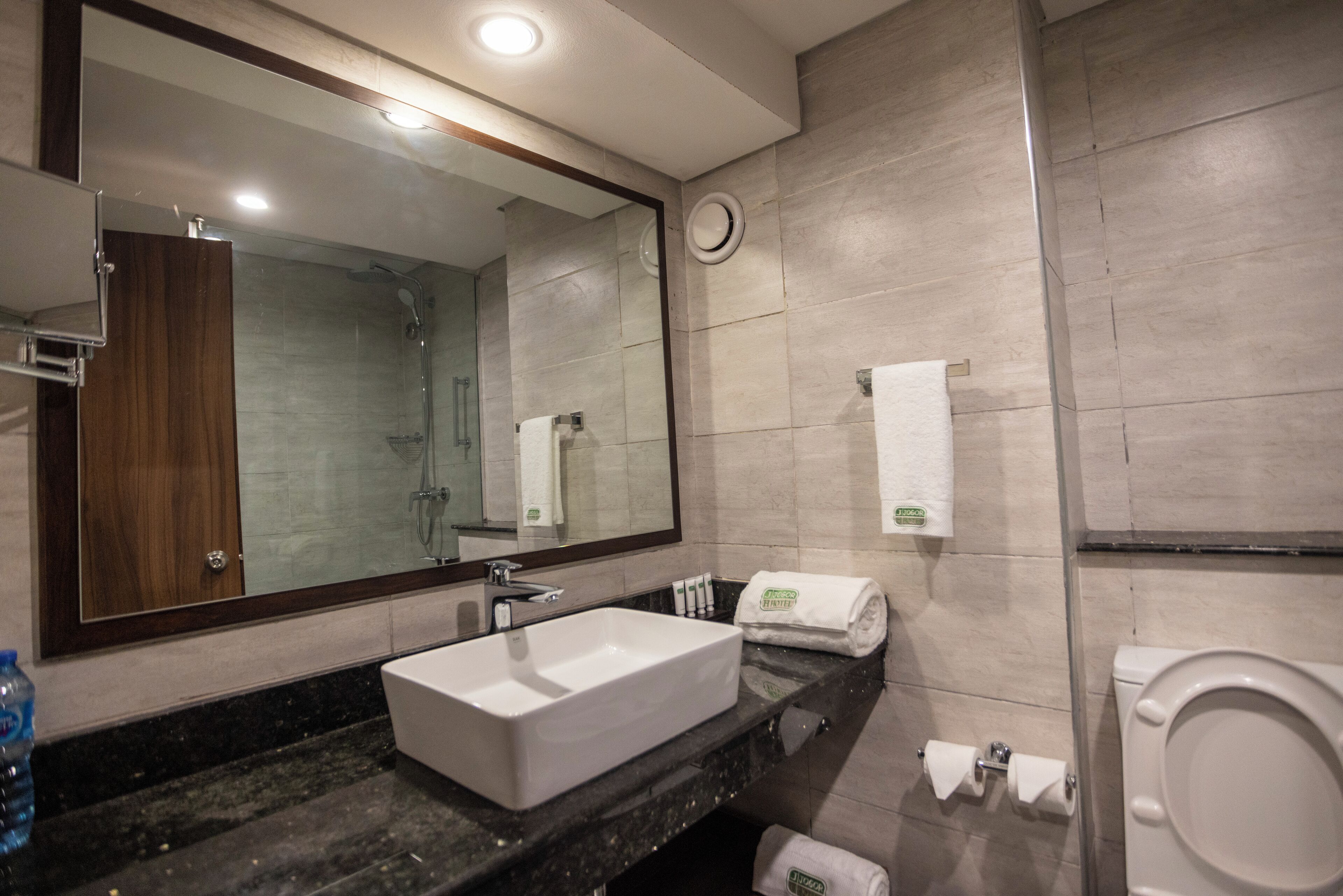 A modern bathroom with a large mirror, a rectangular sink, a toilet, and a shower area.