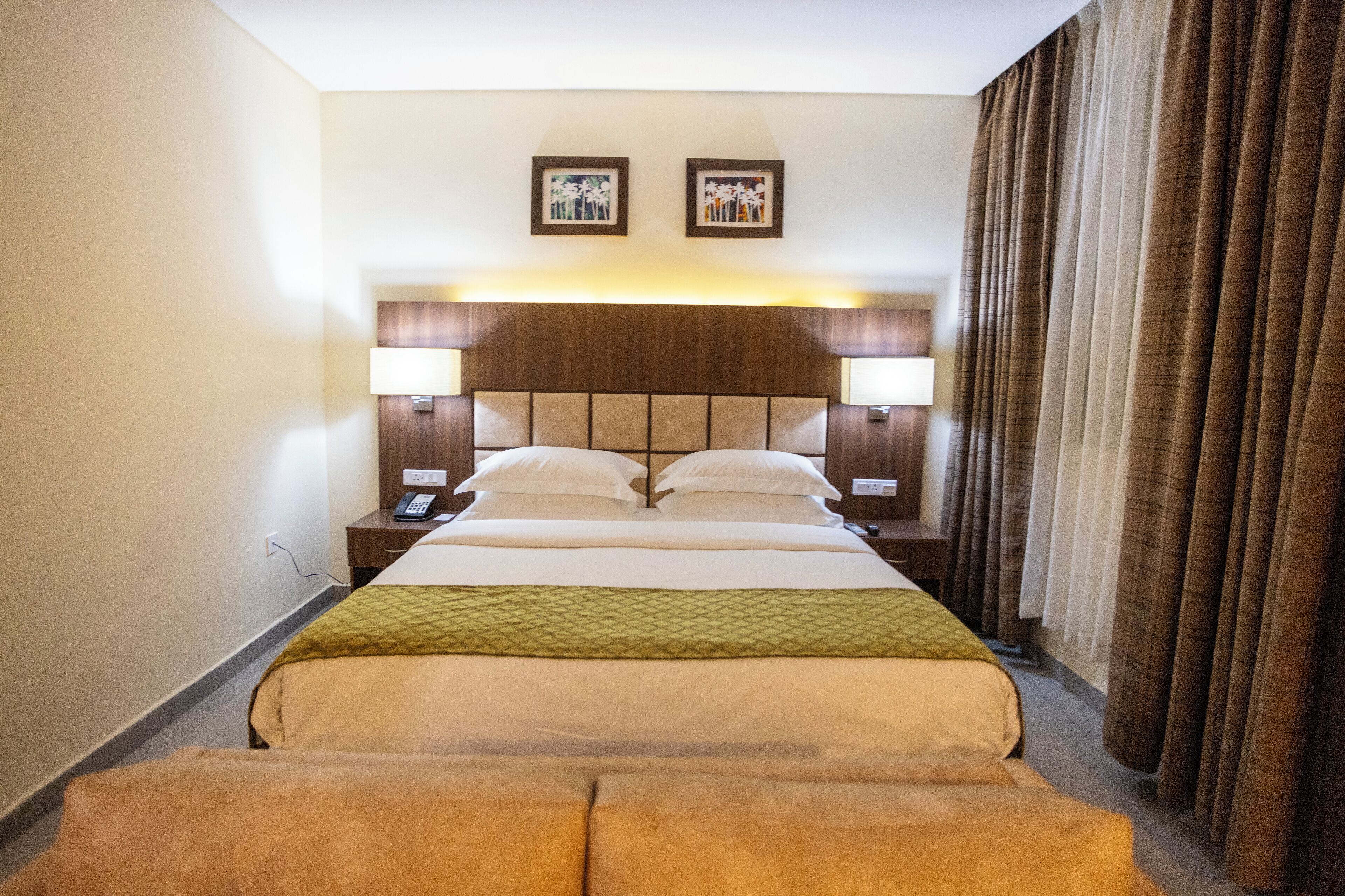 Una habitación de hotel con una cama grande, dos lámparas de noche, cabecera con panel de luz, teléfono y ventana con cortinas.