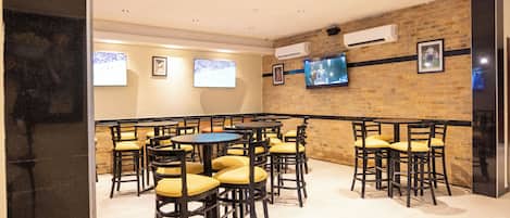 Un restaurante con varias mesas y sillas, un muro de ladrillo y televisores montados.