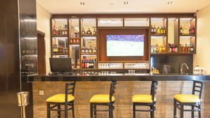 Zona de bar con una pantalla de televisión, varias botellas de licor y tres taburetes con cojines amarillos.