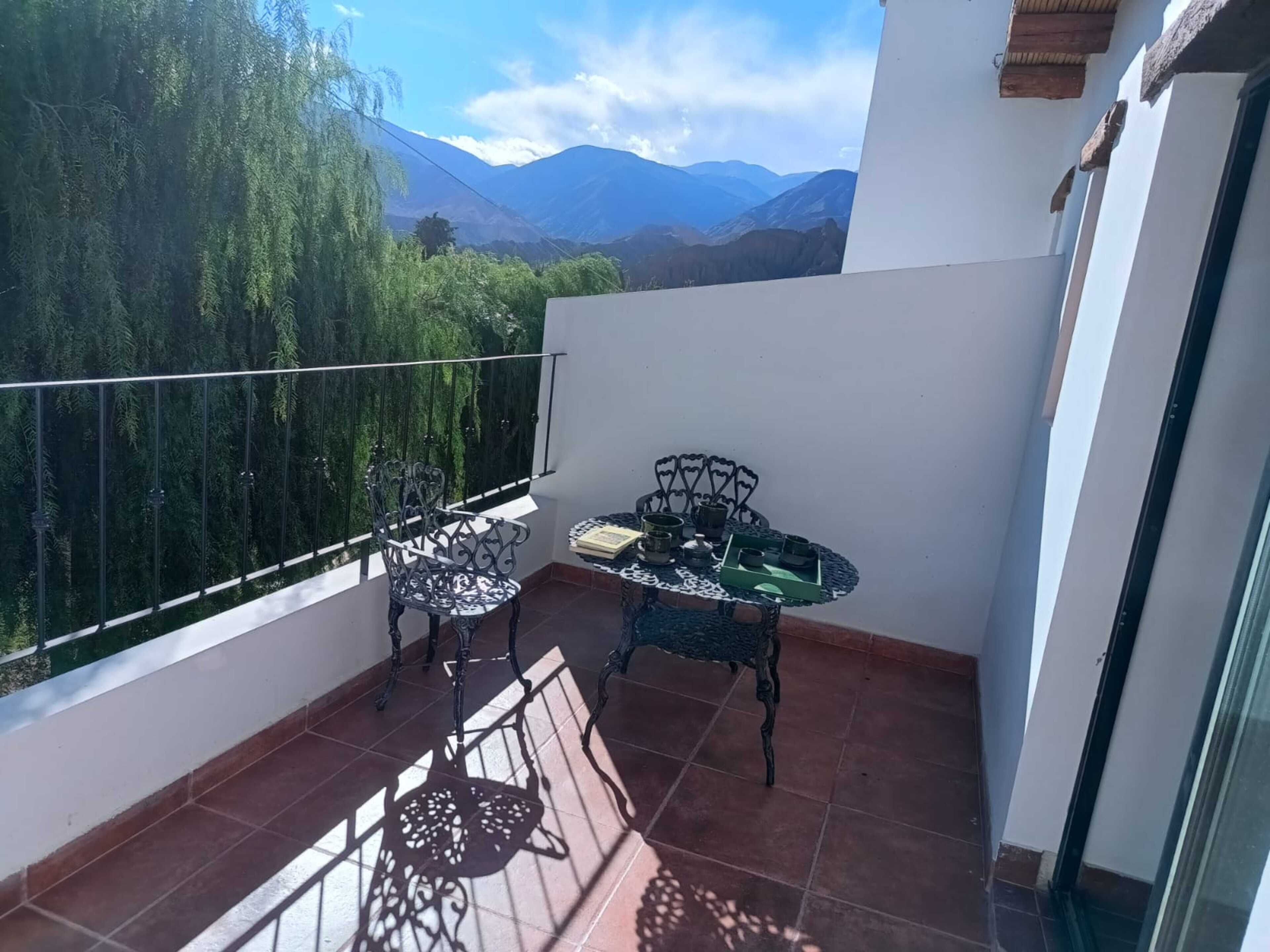 Un balcón con dos sillas y una mesa, vista a las montañas y una puerta de cristal.