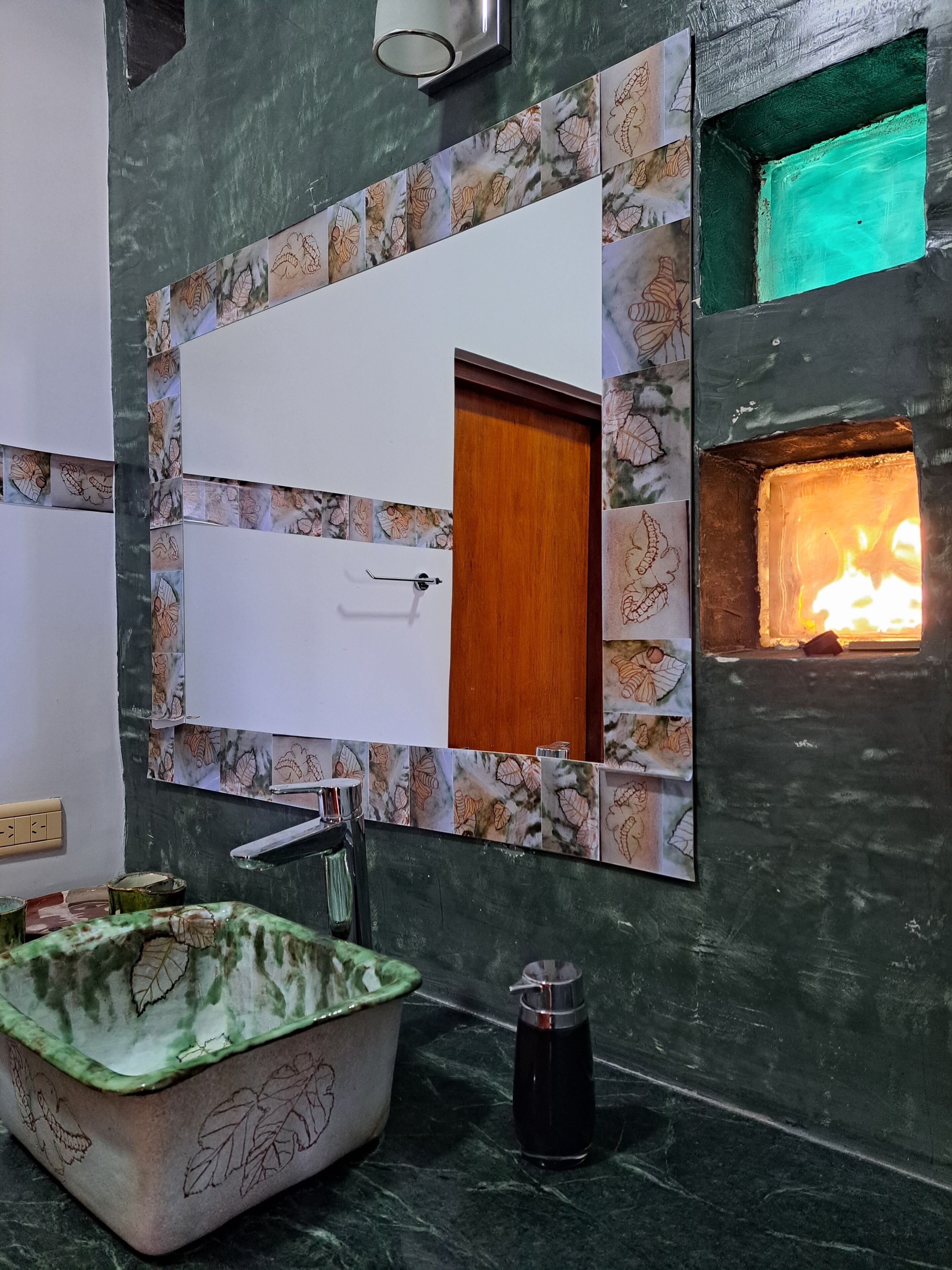 A bathroom with a large mirror, a green bathtub, a sink, and a small fire feature.