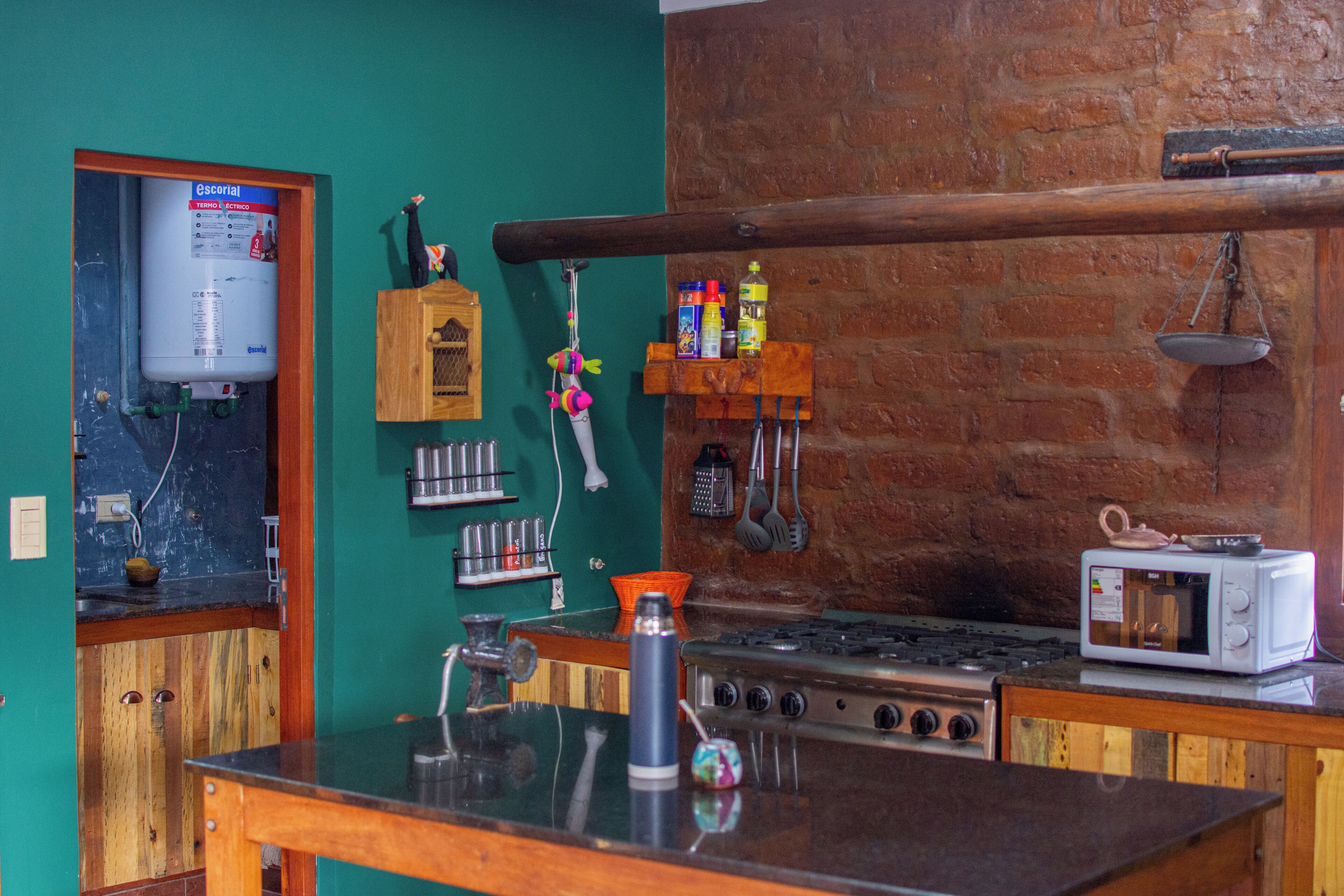 A kitchen with a water heater, a microwave, and a wooden shelf with kitchen utensils.