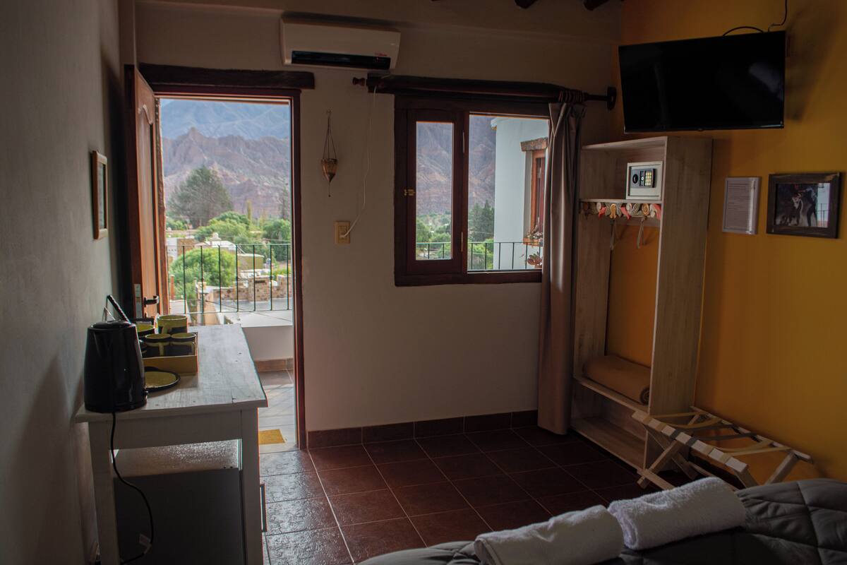 A room with a bed, a TV mounted on the wall, a small table with a coffee maker, and a window with a mountain view.