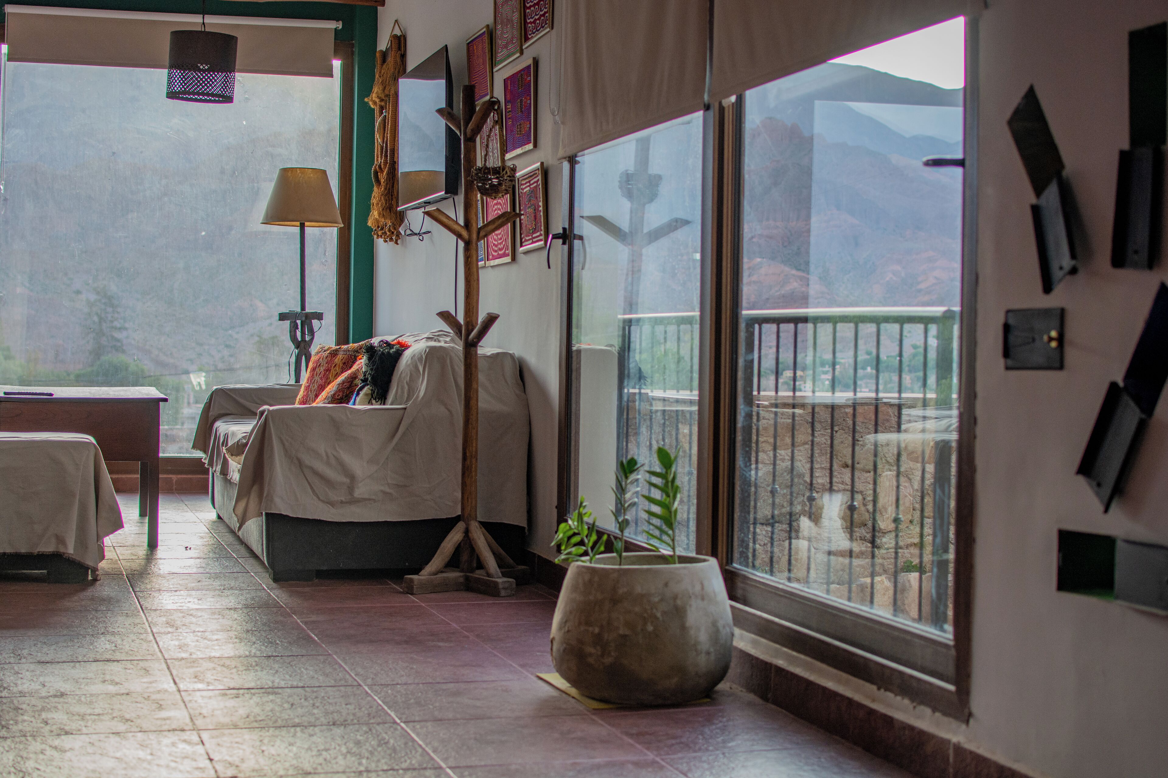 A room with a bed, a desk, a lamp, and a large window with a view of mountains.