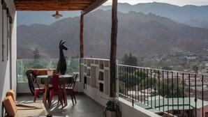 Un balcón con mesa y sillas, una lámpara colgante y vistas a montañas.