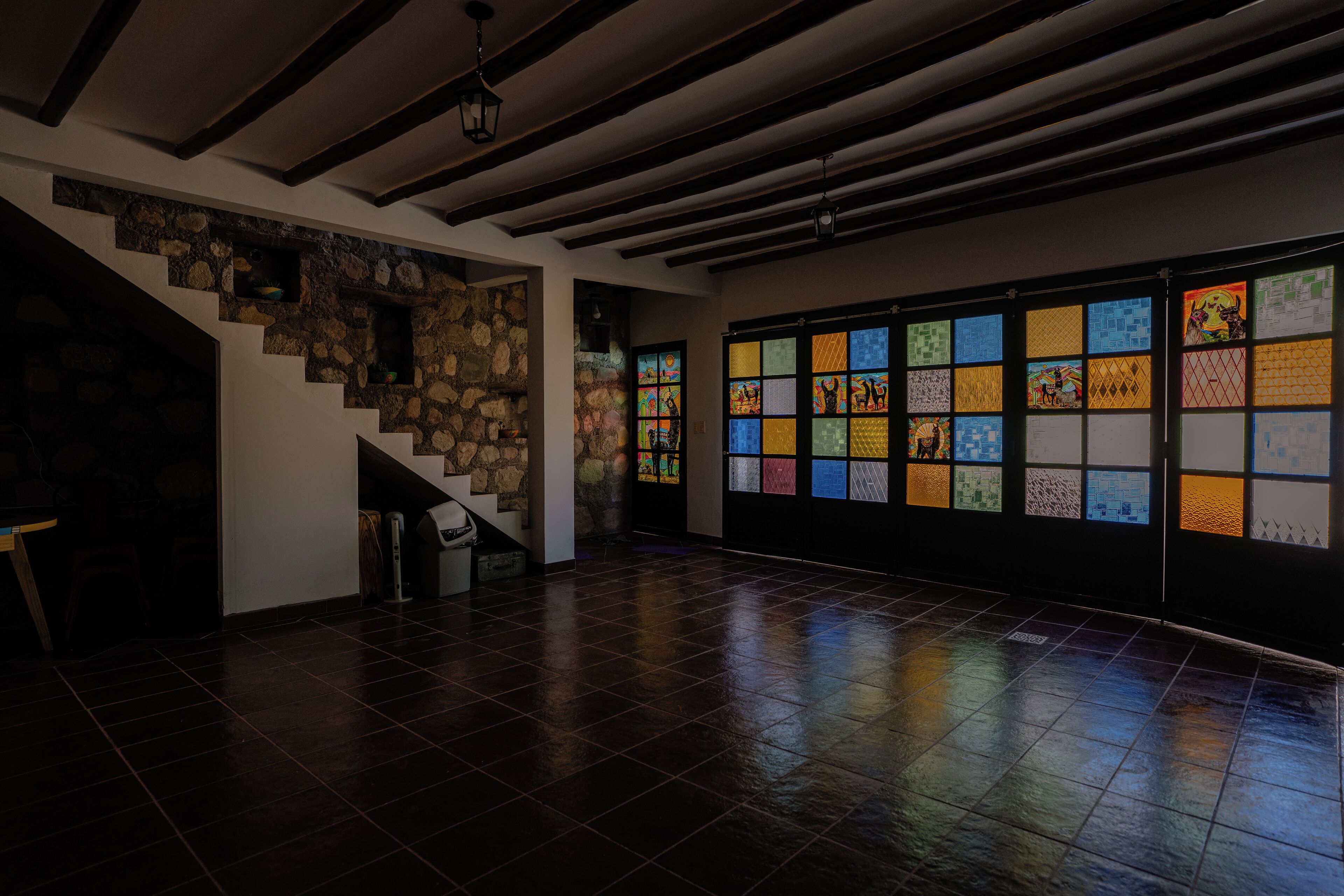 Una habitación espaciosa con piso de baldosas oscuras, pared de piedra y una escalera.